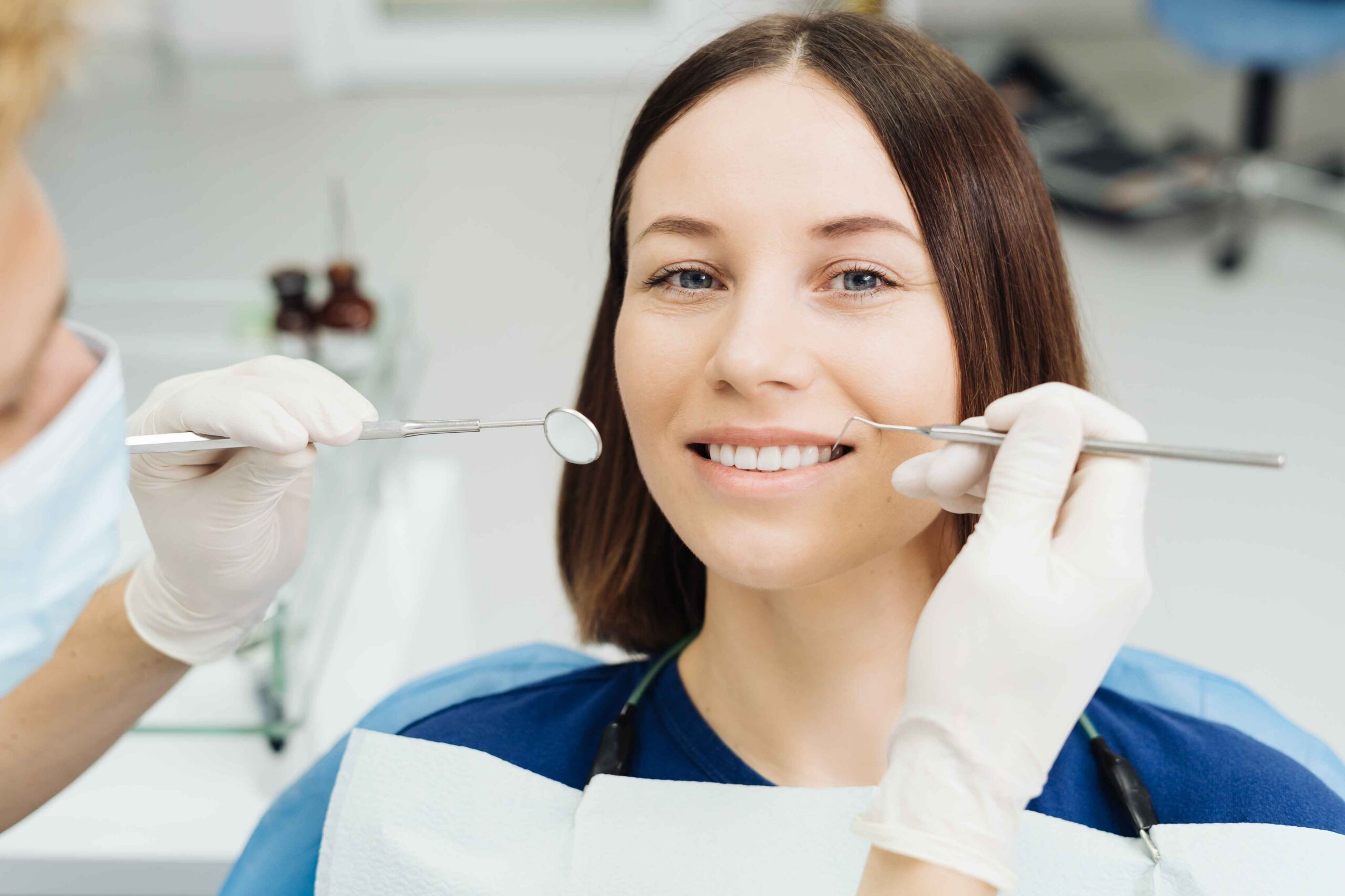 Dentist examining smiling patient's teeth with dental mirror and probe during checkup.