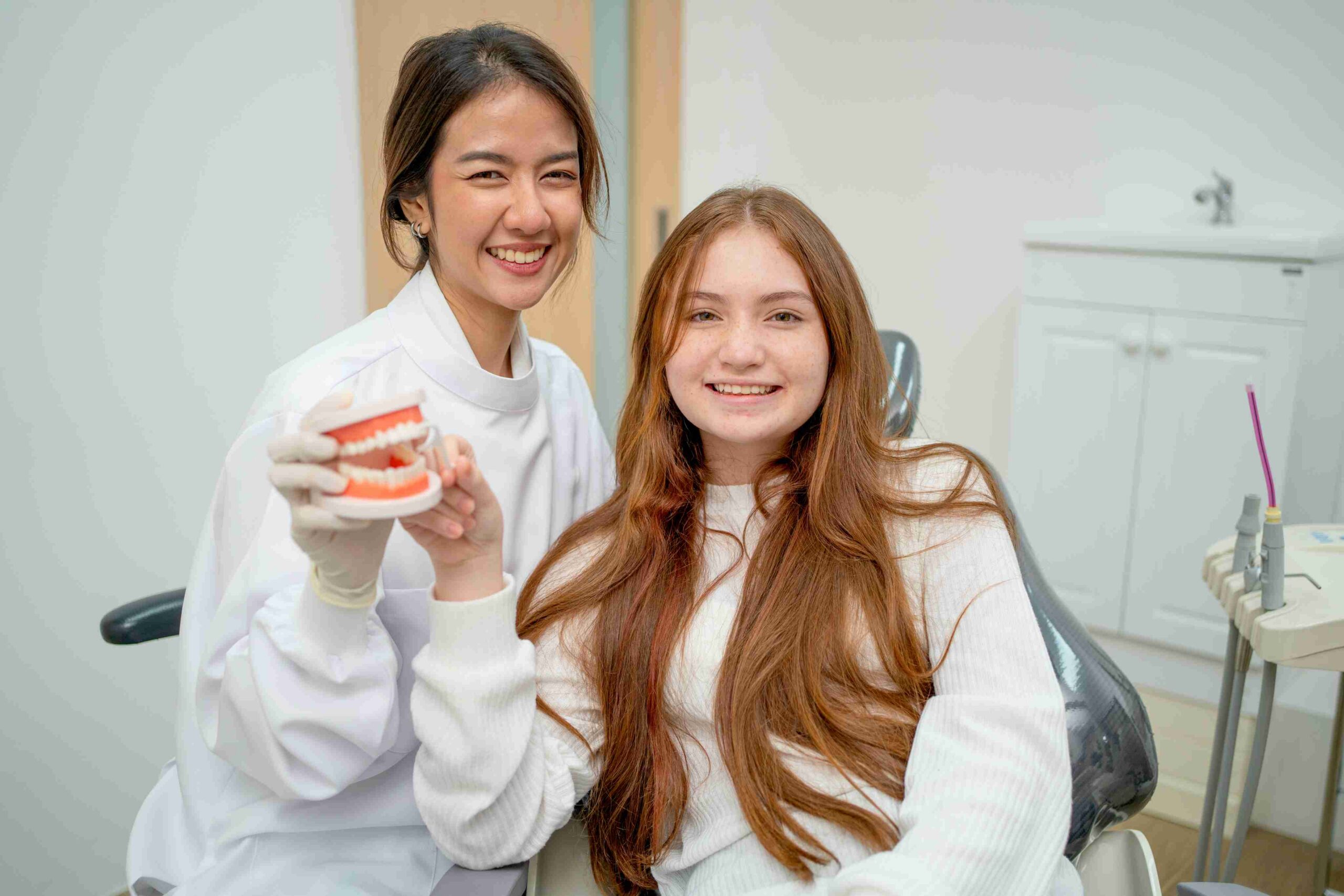 Teen patient and dental professional smiling during a dental consultation with a tooth model.