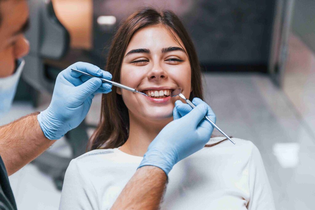 Dentist examining a smiling patient’s teeth with dental instruments during an oral examination.